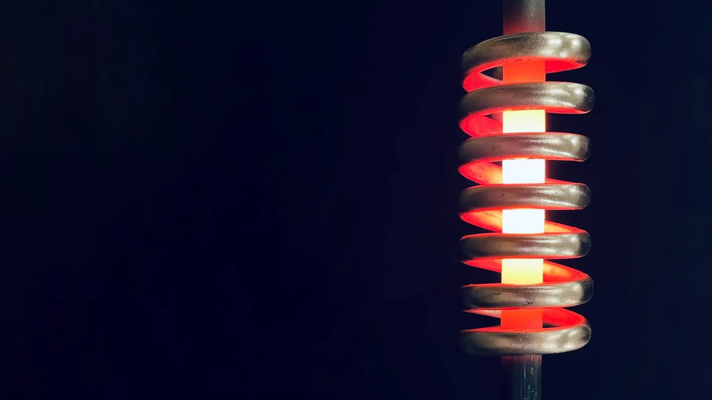 Copper induction coil heating a steel rod until it glows orange and white
